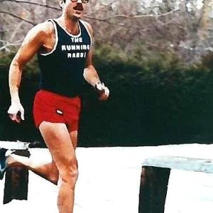Hirshel middle aged white man balding with black glasses and mustache running in a black tank and red short the running rabbi