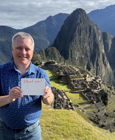 A man holds a card that says 'thank you' in front of Machu Picchu site