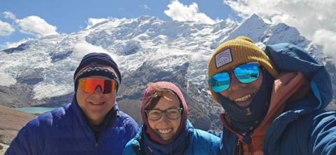 A woman flanked on either side by two men at a mountaintop