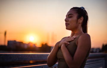 Stock image of woman with hands on chest, breathing, in front of sunset