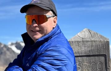 A man with sunglasses stands at a mountain peak at 5,200 meters altitude