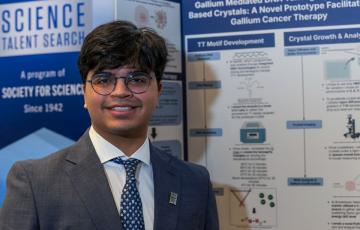 teen researcher stands in front of his project at science competition