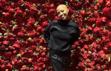 young black woman, bald, dressed in black in front of red roses