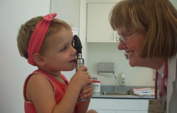 Little girl with red headband and shirt holding medical instrument next to a woman with glasses