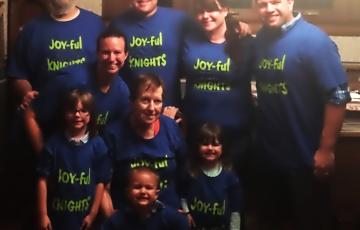 Six adults and three children all wearing blue shirts that say Joy-ful Nights