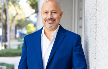 balding middle aged hispanic man with graying beard and mustache smiling and wearing a royal blue jacket and white shirt