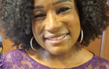 middle aged black woman wearing hoop earrings and a purple lace dress.