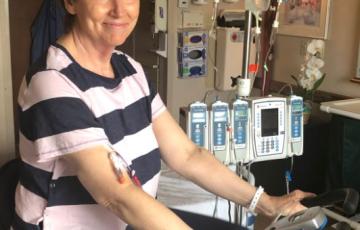 middle aged white woman with short brown hair wearing a navy and pink striped blouse and blue pants riding a stationary bike in a hospital room