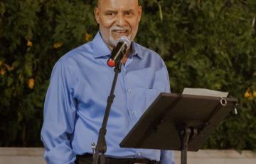 older balding man wearing a blue shirt standing in front of a microphone and podium