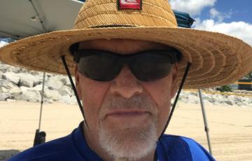 older white man with beard and mustache wearing sunglasses a strawhat and blue t-shirt