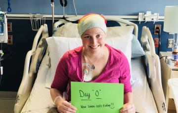 young white woman in a hospital bed wearing a pink shirt, turban and holding a green sign that says new stem cells today