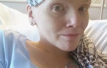 young white woman with a scarf on her bald head wearing a blue shirt laying in a hospital bed