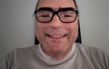 middle aged balding hispanic man with bushy eyebrows wearing black glasses and an Oktoberfest t-shirt