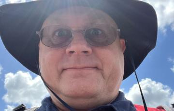 middle aged white man with glasses and a black hat wearing a red and navy shirt with a Walt Disney World nametag.
