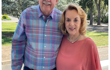 older white balding man with glasses and blue plaid shirt with older white woman with blond hair necklace and pink blouse