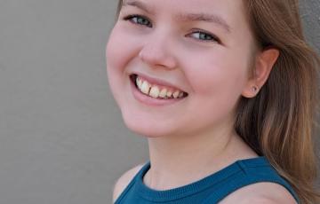 young white girl with brown hair and star earrings with a slight gap in her two front teeth wearing a blue tank top