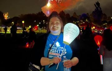 young white girl with her hair pulled up with glasses wearing a black jacket and blue tshirt carrying a white balloon at LTN with fireworks in the background