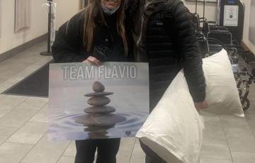 Flavio young hispanic couple she is holding Team Flavio poster and he is holding a pillow both wearing black jackets