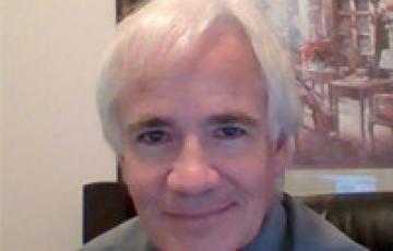 James older white man with white hair wearing a shirt and tie sitting in front of framed artwork