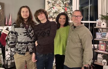 John William middle aged white man wearing glasses and a gray shirt standing in front of Christmas tree with his wife in a green sweater and two sons