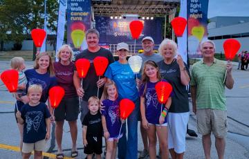 Tricia young white woman wearing a khaki ball cap and blue t-shirt and jeans holding a white LTN balloon surrounded by adutls and children holding orange balloon at a LTN walk