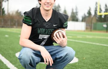 young adult smiling while holding a football on the field wearing a jersey