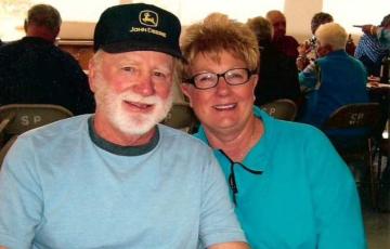 myeloma patient older white man with white beard and mustache wearing John Deere hat and blue tshirt with wife with short hair glasses and turquoise shirt