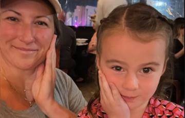 young white woman wearing ball cap and greenish tshirt with daughter in a pink and black top and both have a hand up against their cheeks