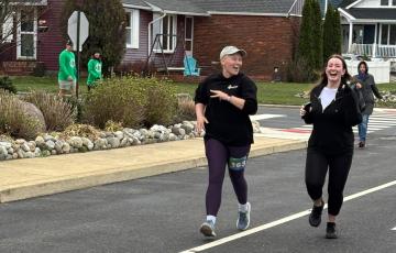 Ally two young white women running along a street one bald and wearing a ball cap both in dark running gear