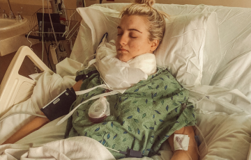 Brescia young white woman laying in a hospital bed with blond hair pulled into a pony tail on top of her head eyes closed wearing green leaf hospital gown